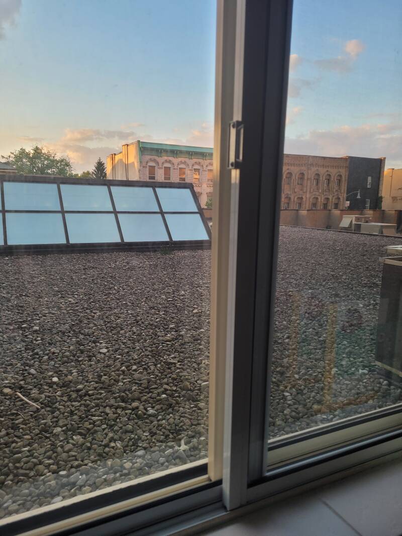 picture from a window of a roof top apartment showing rock covered roof top glass dome winows over a mall and buildings across the street