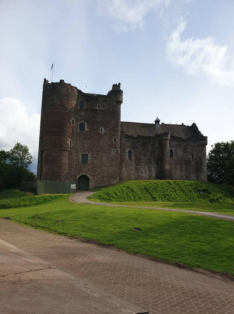 Doune Castle, the real-life filming location of Castle Leoch in Outlander, photographed on a clear day with lush green grass and blue sky.