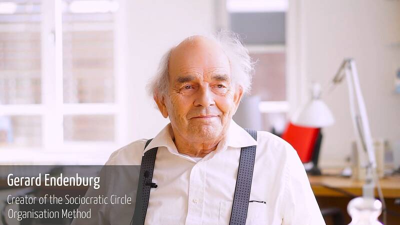 Afbeelding van Gerard Endenburg, in een licht kantoor, vanaf de borst met een wit overhemd en grijze bretels. Hij kijkt vriendelijk naar rechts van de camera. Afbeeliding van Charlie Shread.