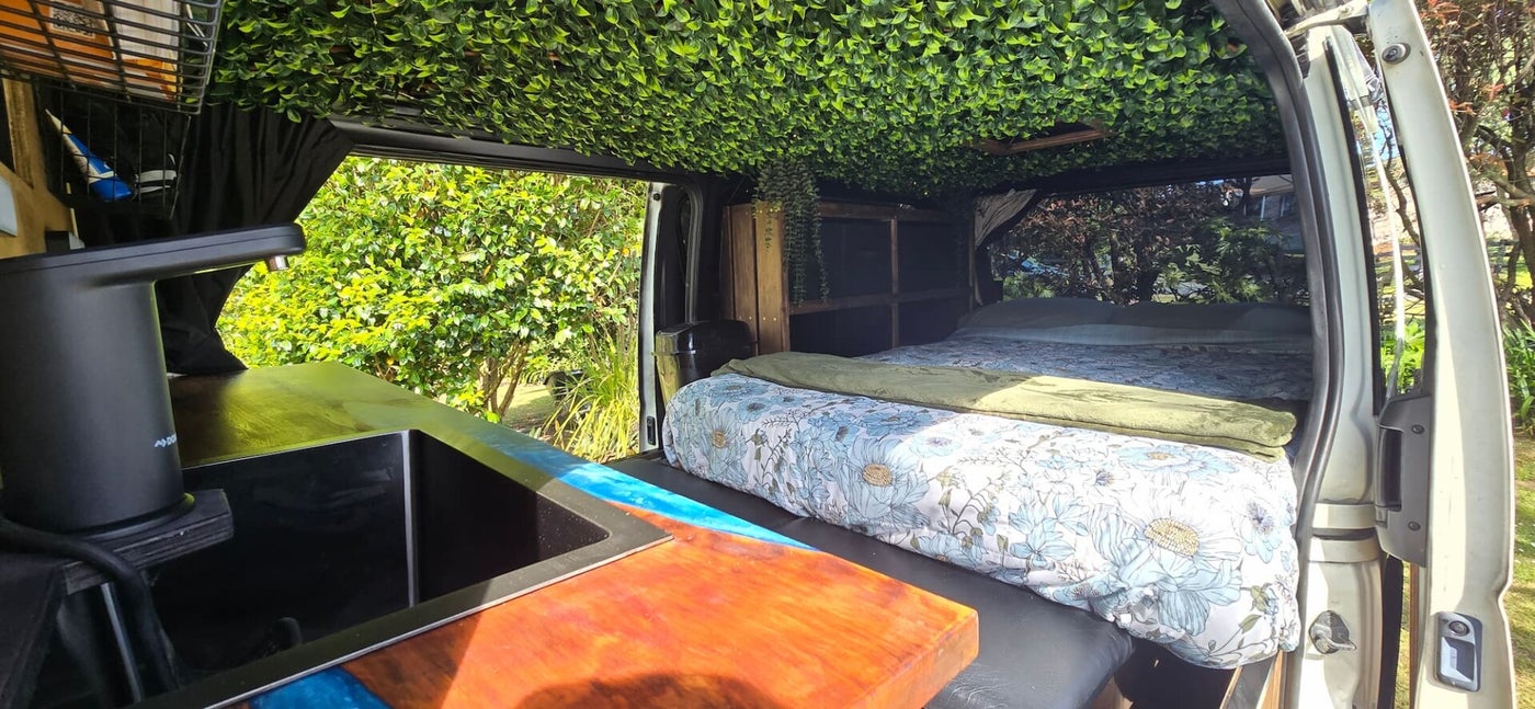Interior view of Demeter luxury campervan showing cozy bed, fairy lights, and rich timber finishes