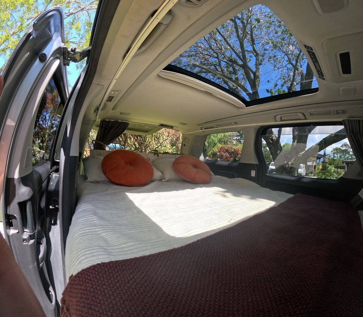 Hestia luxury campervan interior featuring a massive open sunroof, plush queen bed, and premium timber finishes