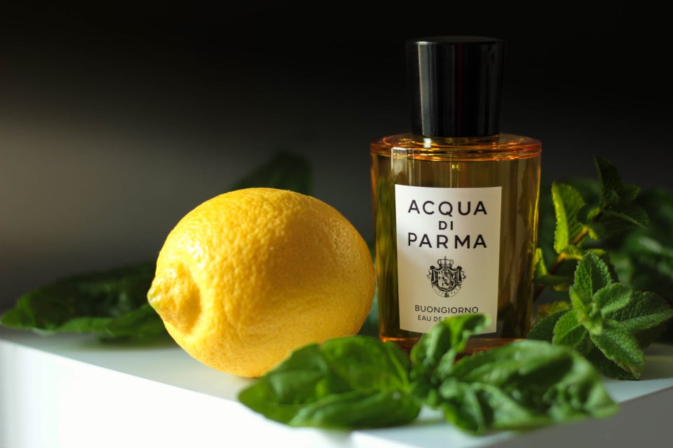 Fresh lemon and green herbs next to Acqua di Parma fragrance bottle