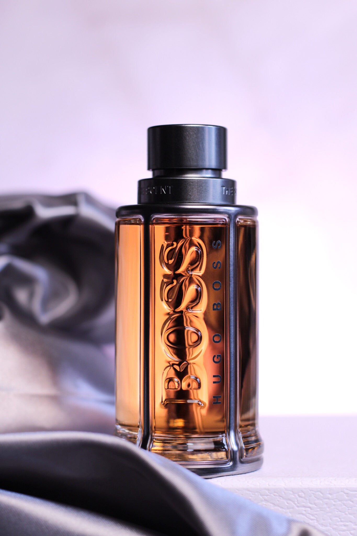 Product shot of Hugo Boss The Scent EDT with silver satin fabric and pastel background