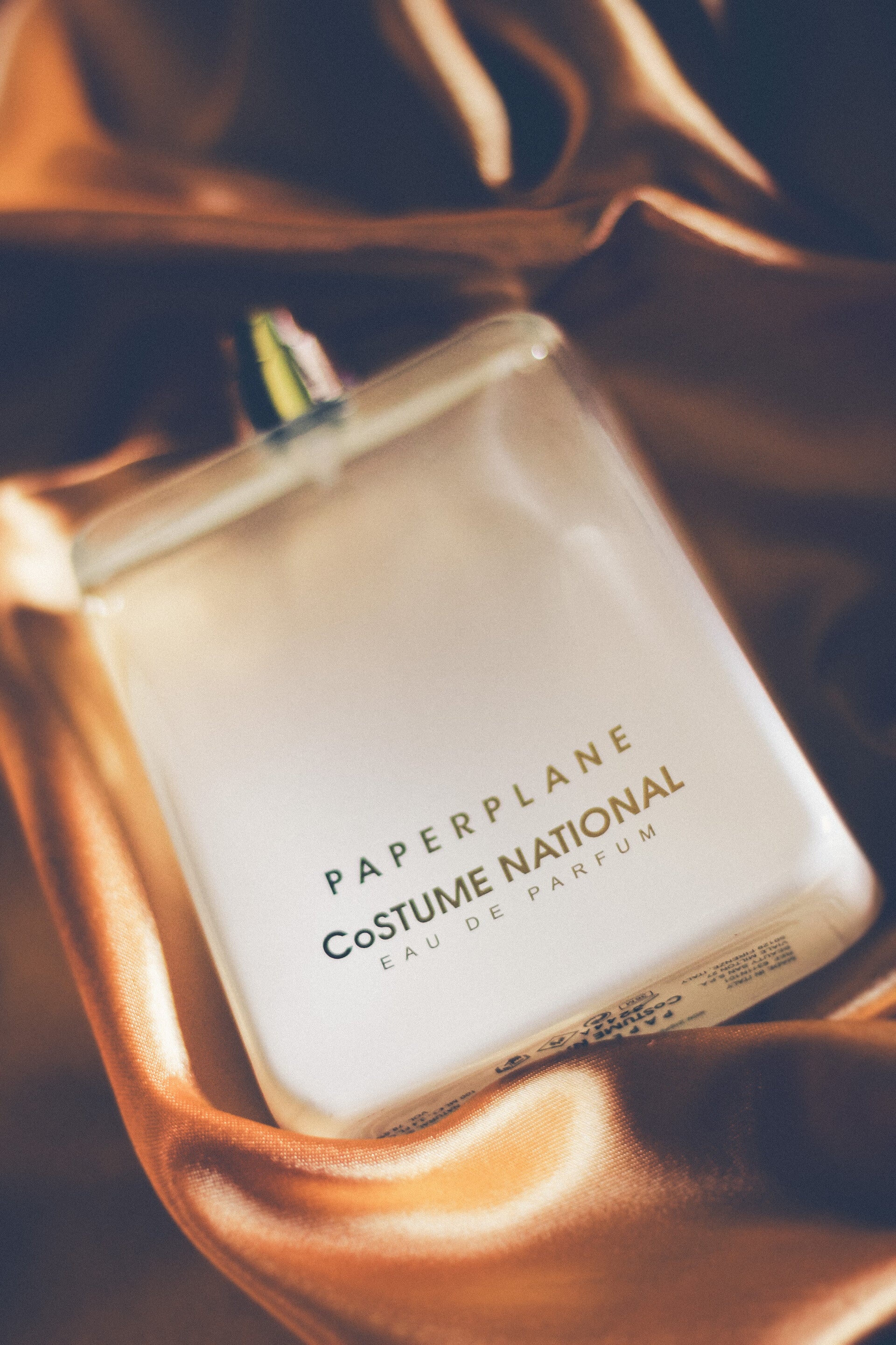 Close-up of CoSTUME NATIONAL Paperplane Eau de Parfum resting on glowing silk.