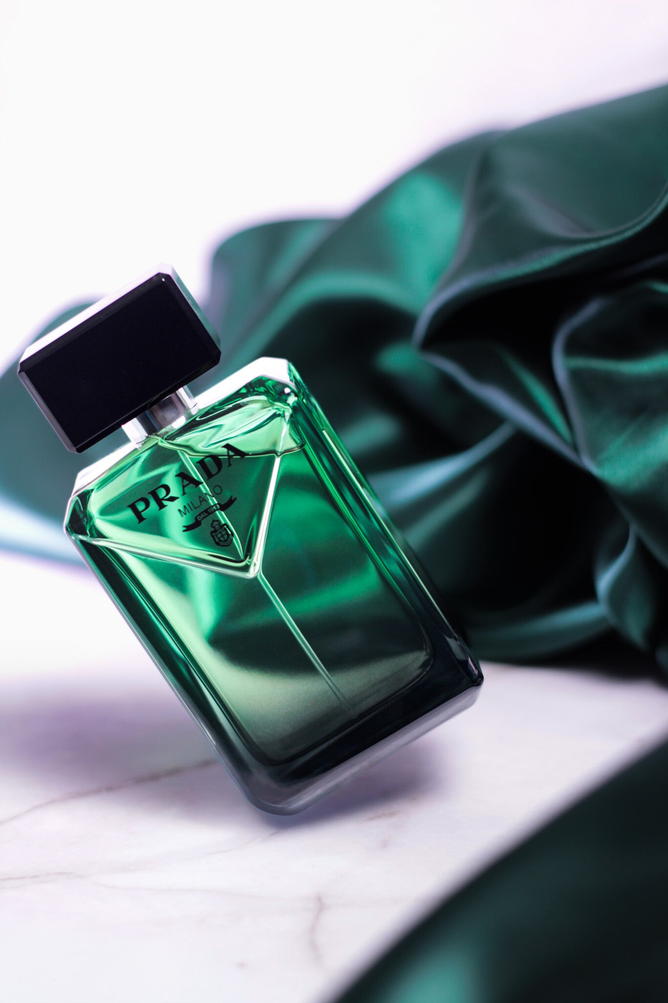 Elegant shot of Prada Paradigme eau de parfum with green reflective bottle and draped fabric background.