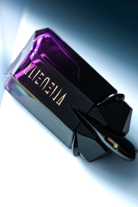 Elegant flatlay of Mugler Alien Extraintense bottle with gold lettering and dark gradient background