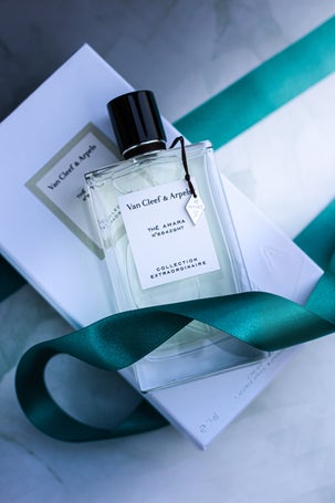 Flat lay of Van Cleef & Arpels Thé Amara Eau de Parfum with soft lighting, teal ribbon, and marble texture.