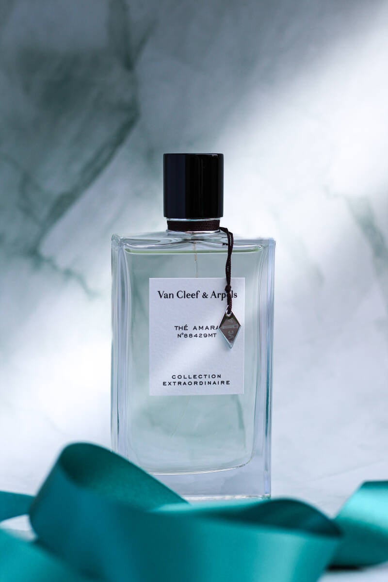 Minimalist product shot of Van Cleef & Arpels Thé Amara fragrance with decorative green ribbon on stone background.