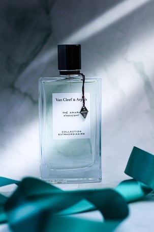 Minimalist product shot of Van Cleef & Arpels Thé Amara fragrance with decorative green ribbon on stone background and shadows