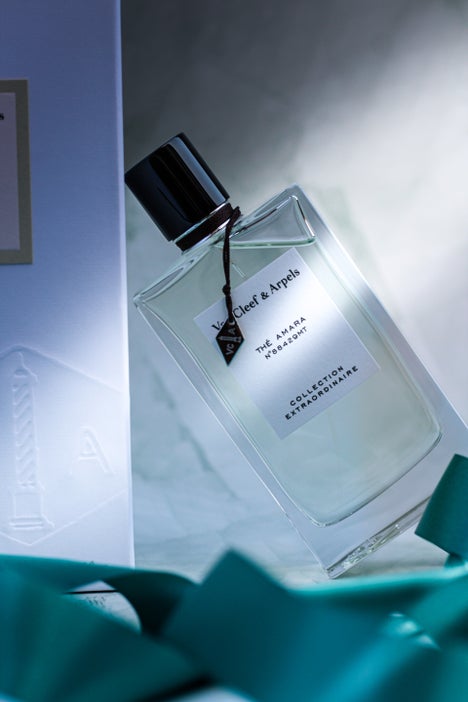 Minimalist product shot of Van Cleef & Arpels Thé Amara fragrance and box, with decorative green ribbon on stone background.