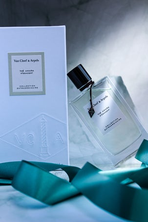 Van Cleef & Arpels Thé Amara in a clear rectangular bottle, styled on a marbled surface with satin teal ribbon for an elegant look.
