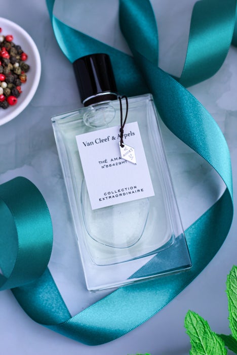 Bottle of Van Cleef & Arpels Thé Amara Eau de Parfum from the Collection Extraordinaire, placed on a marble background with a teal satin ribbon, with mint leaves and pepper