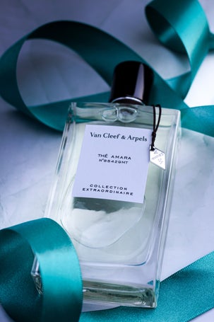 Bottle of Van Cleef & Arpels Thé Amara Eau de Parfum from the Collection Extraordinaire, placed on a marble background with a teal satin ribbon and shadows