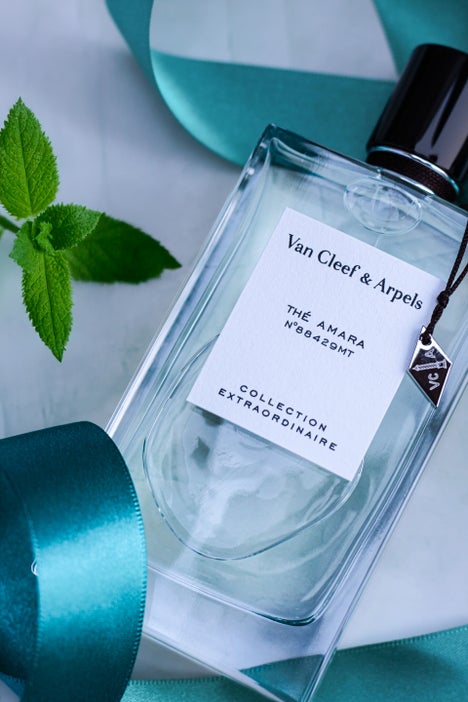 Bottle of Van Cleef & Arpels Thé Amara Eau de Parfum from the Collection Extraordinaire, placed on a marble background with a teal satin ribbon and fresh mint leaves
