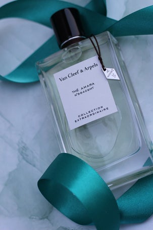 Elegant bottle of Thé Amara by Van Cleef & Arpels from the Collection Extraordinaire, styled with teal ribbon on a marble background.