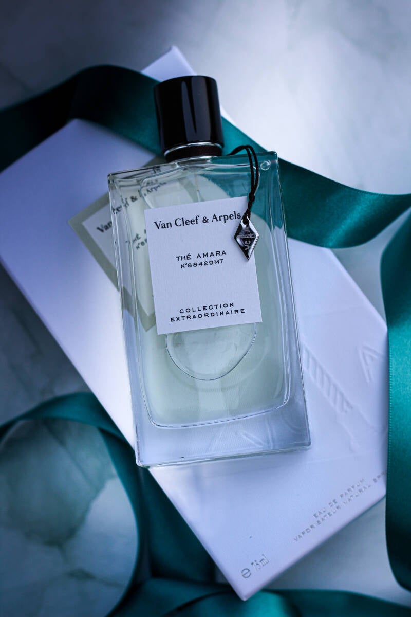 Elegant bottle of Thé Amara by Van Cleef & Arpels from the Collection Extraordinaire, styled with teal ribbon on a marble background with some shadows