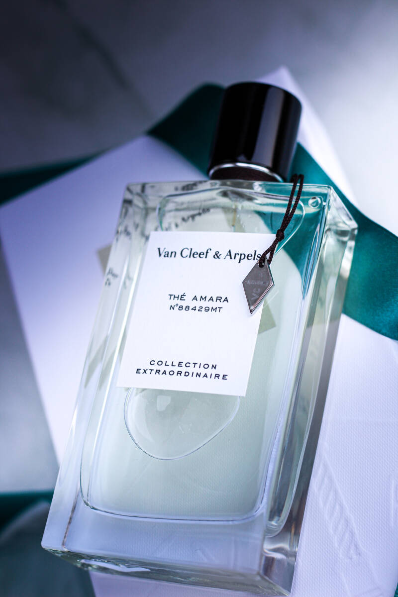 Close up of the elegant bottle of Thé Amara by Van Cleef & Arpels from the Collection Extraordinaire, styled with teal ribbon on a marble background.