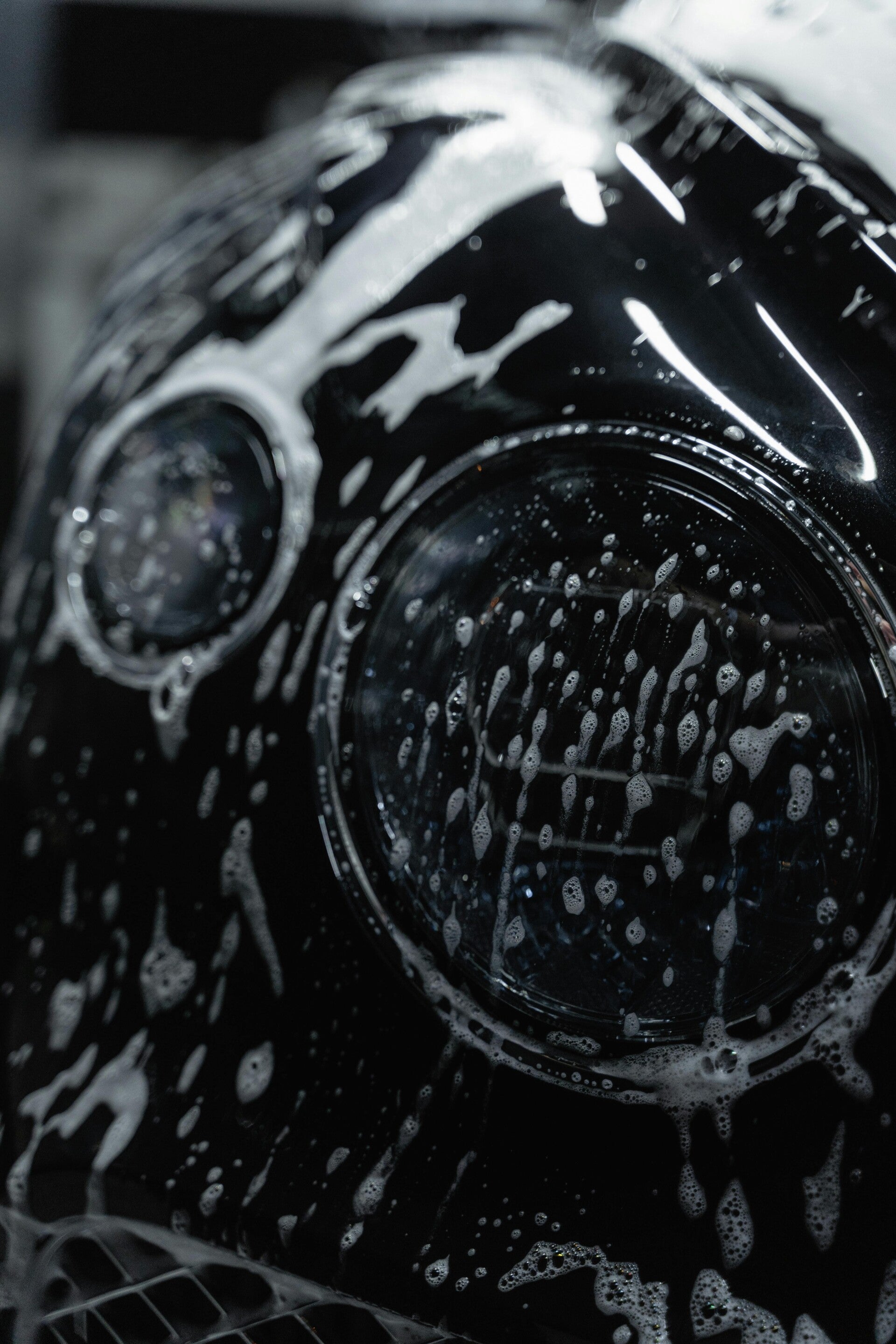 a close up of a black cars headlight with soap and water on it from an exterior service