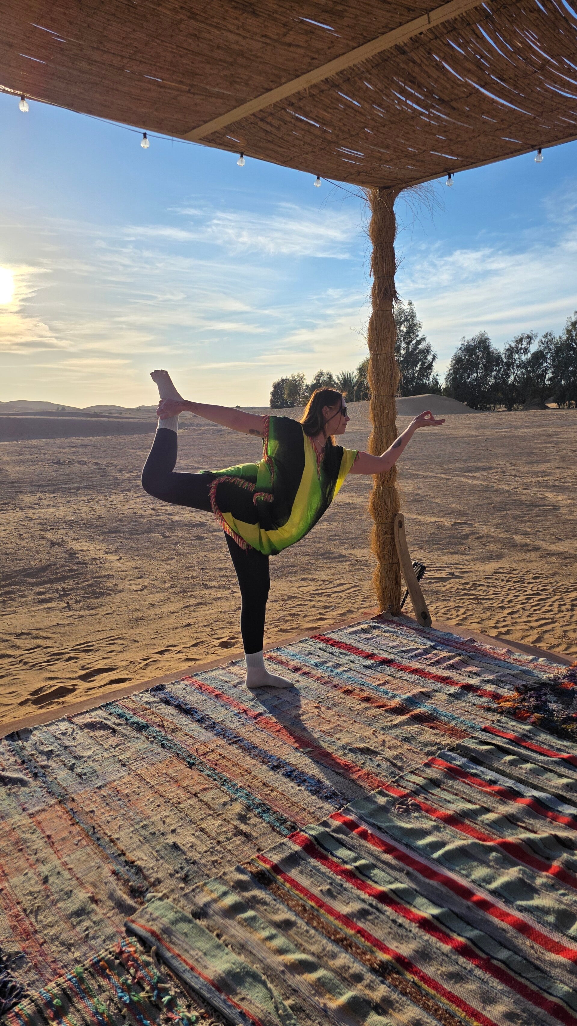 Practicing the dancer yoga pose at the desert yoga platform in Morocco, wearing traditional desert attire at a luxury Sahara retreat