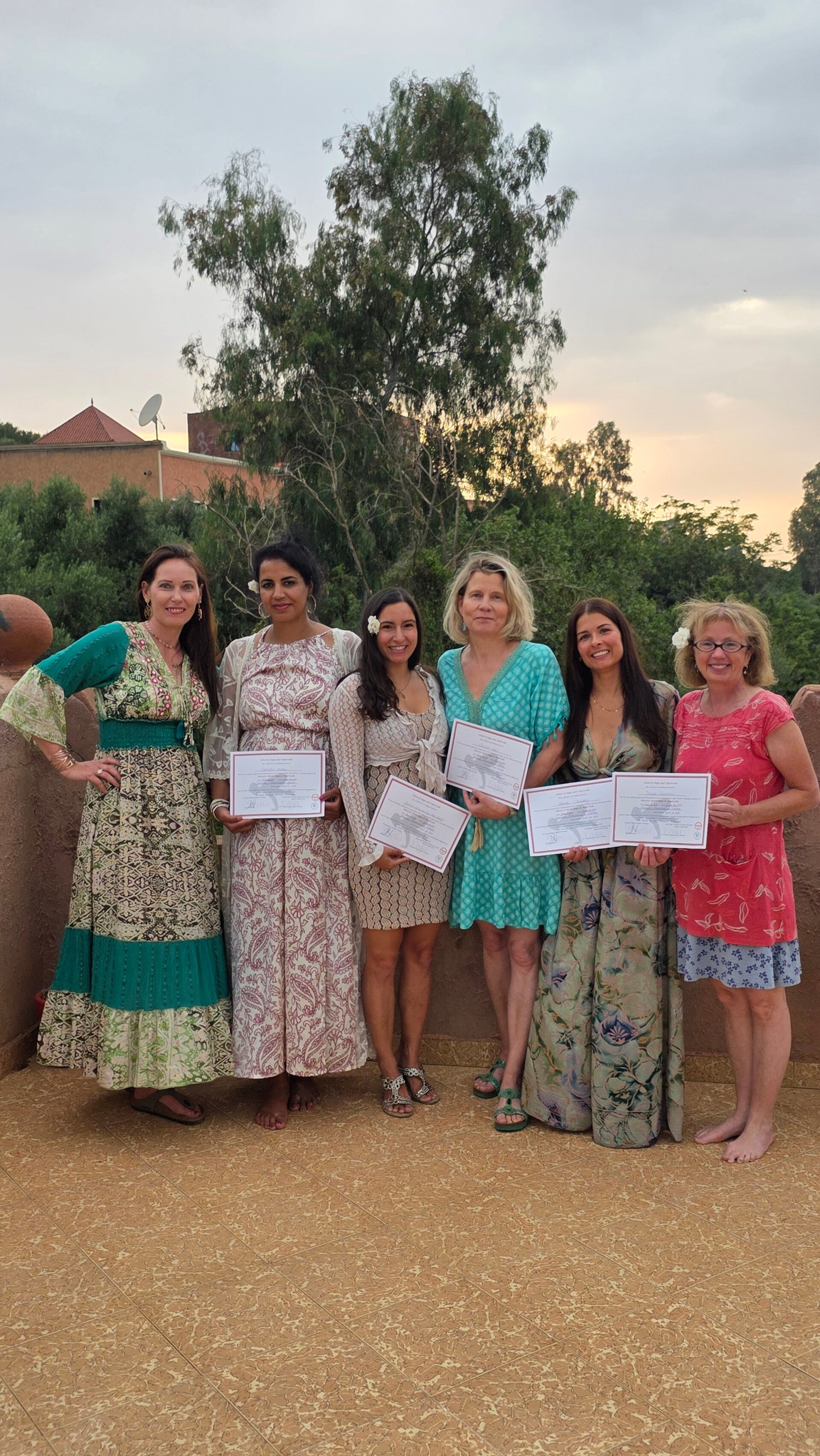 Yin Yoga Teacher Training Morocco graduation ceremony with students holding certificates on a Marrakech rooftop terrace at sunset