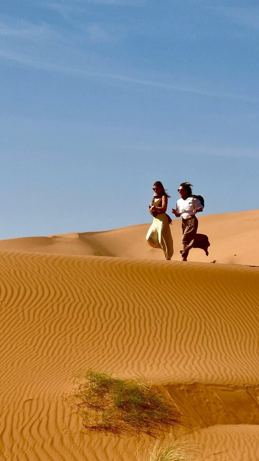 Two women walking on the golden dunes of Merzouga at sunrise during the New Year Yoga & Desert Retreat in Morocco with Nella Retreats.