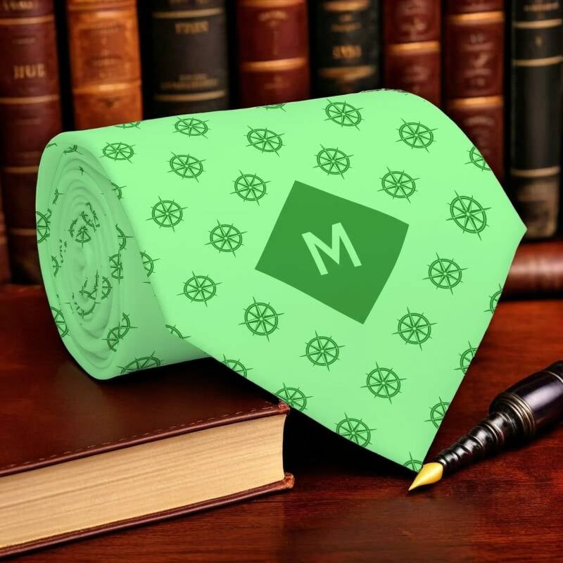A lime green necktie adorned with a pattern of nautical compass symbols and a monogrammed M on the diamond-shaped dark lime green background.