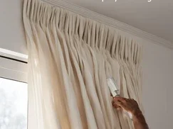 "A person using a vacuum attachment to clean elegant drapes, highlighting the professional drapery cleaning services provided by Tegridy Carpets for maintaining fresh and dust-free curtains."
