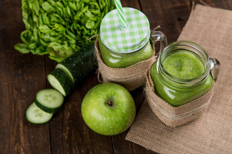 Two Jars of Green Smoothies with green leavy vegetable, green apple and cucumber slices