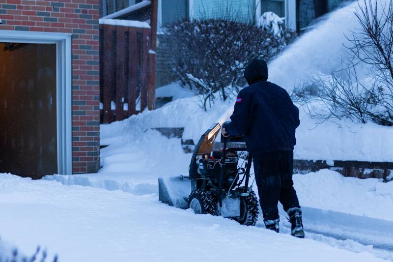 Déneigeur utilisant une souffleuse devant une résidence enneigée