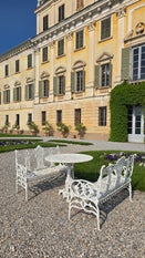 Villa Bettoni in Bogliaco am Gardasee, Außenansicht im Vordergrund Tisch und zwei Bänke aus weißem Metall, im Hintergrund die gelbe Fassade der Villa Bettoni