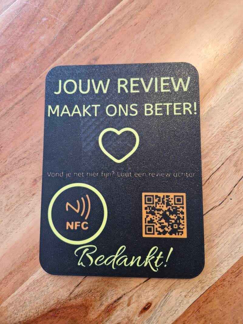 Een zwarte reviewkaart met QR-code, NFC-icoon en de tekst 'Jouw review maakt ons beter', gefotografeerd op een houten ondergrond