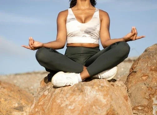Woman sitting cross-legged on a rock in meditation pose, practicing mindfulness outdoors.