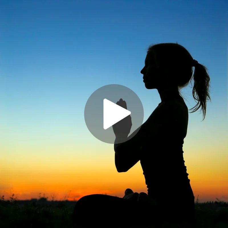 Femme méditant en silhouette devant un ciel au coucher du soleil.