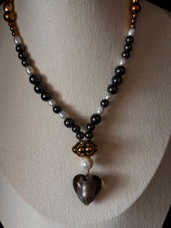Ketting van hematiet, witte parels en goudkleurige elementen met een gouden kraal en een hartje van glas