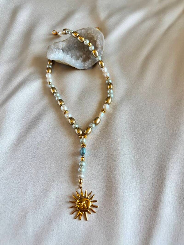 Parelketting met goudkleurige elementen en bedel van een zon.