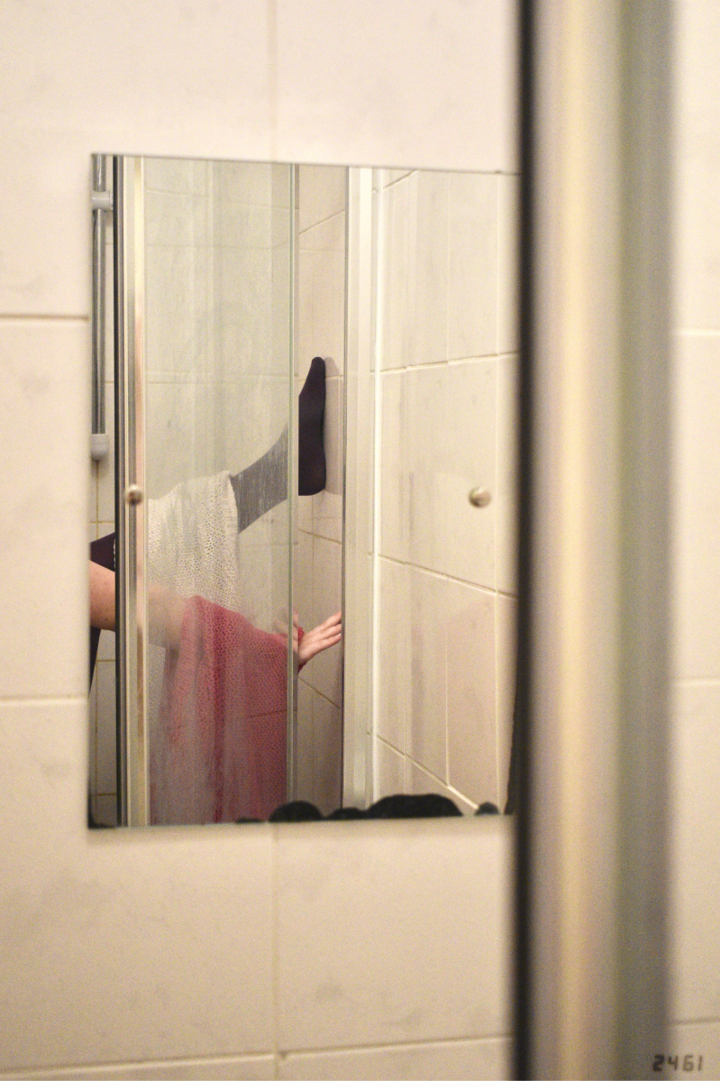 Bathroom mirror with leg in purple tights, pale-skinned arm, and white and pink jumpers