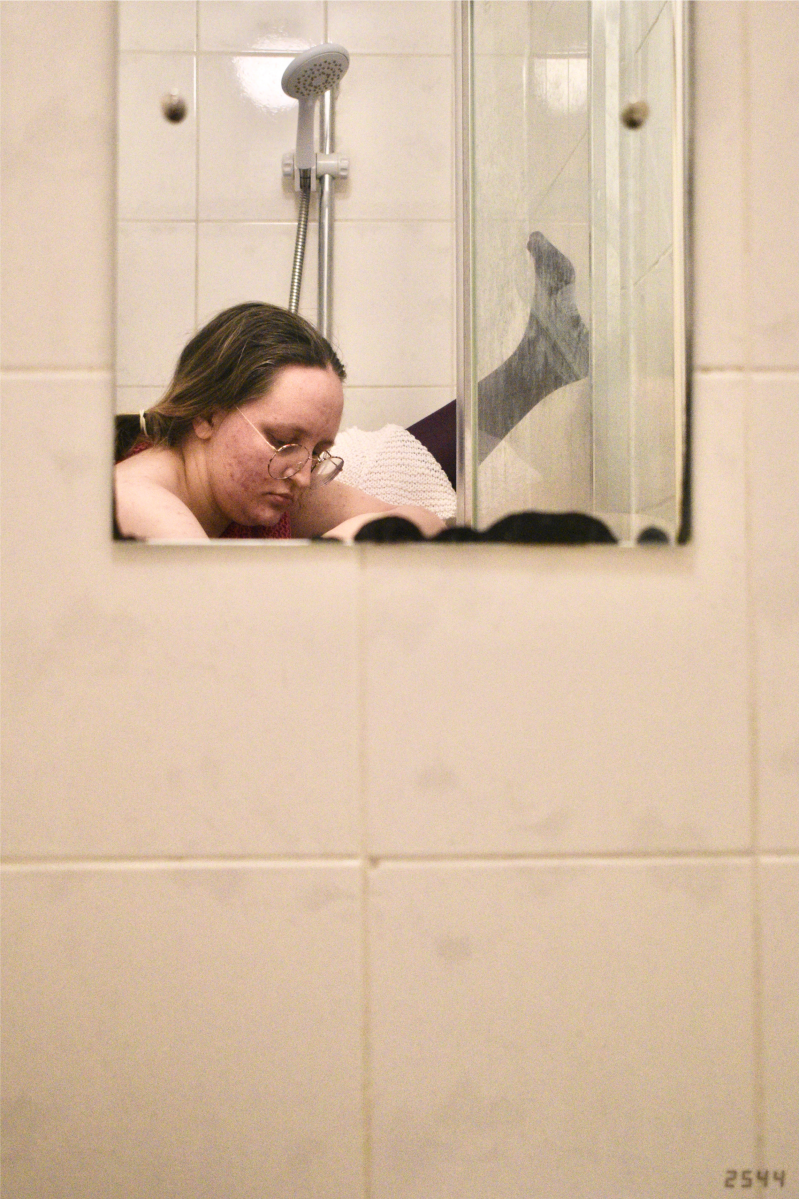 Bathroom mirror with leg in purple tights, pale-skinned arm, and white and pink jumpers
