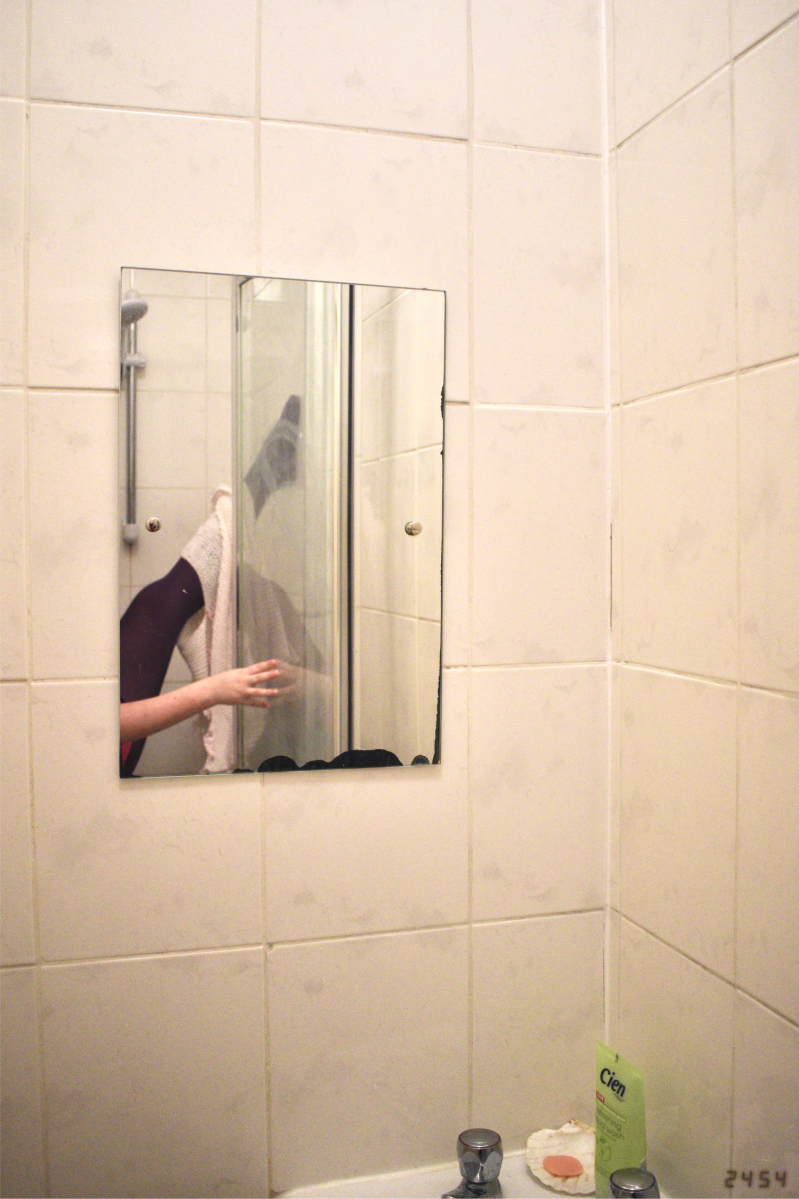 Bathroom mirror with leg in purple tights, pale-skinned arm, and white and pink jumpers