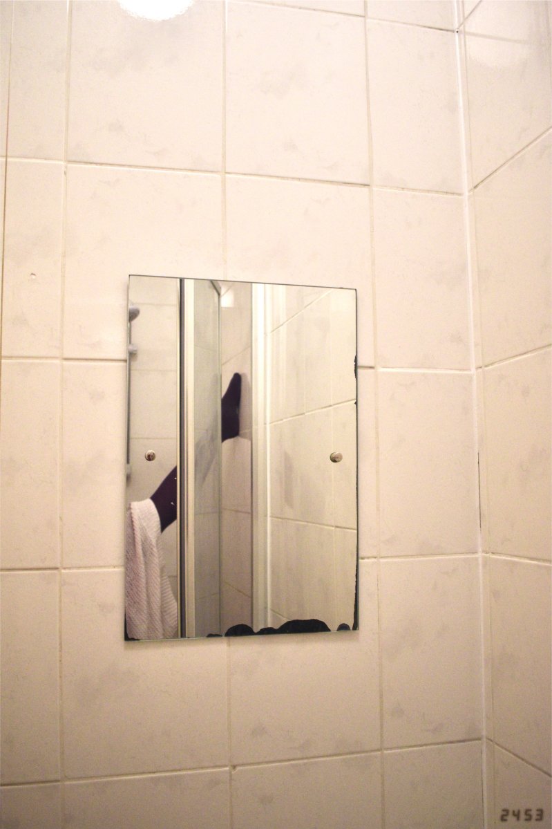 Bathroom mirror with leg in purple tights, pale-skinned arm, and white and pink jumpers