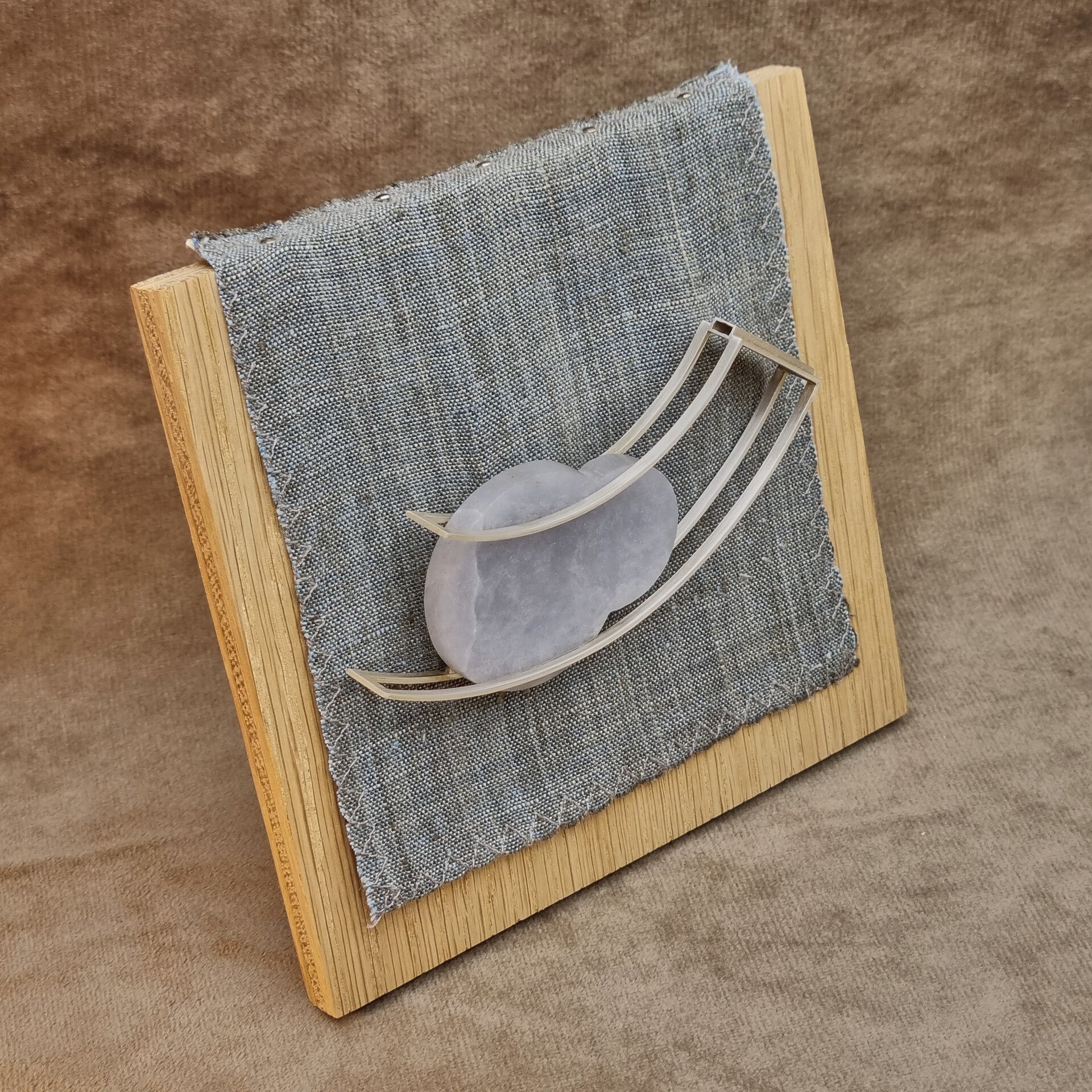 This brooch features a sterling silver frame, blue alabaster, and a nickel-silver brooch pin, displayed on an oak and linen stand.