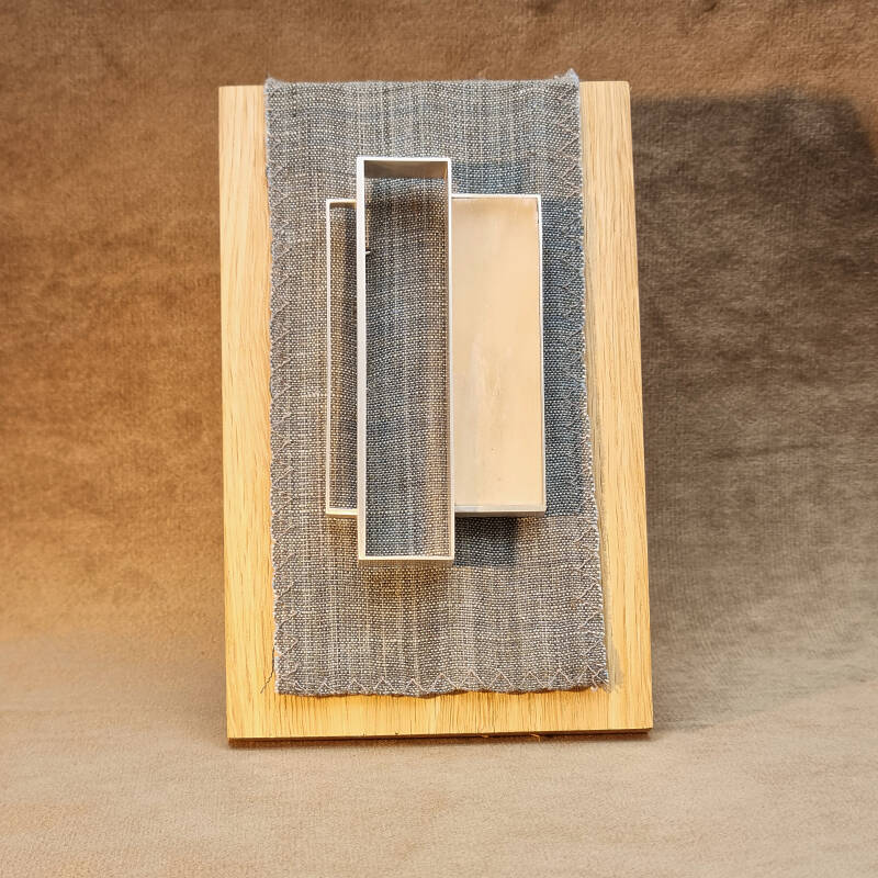 Deze broche is gemaakt van sterling zilver, perzikseleniet en een stalen brochespeld op een standaard van eikenhout en linnen.