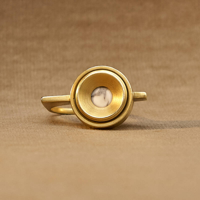 Een ring van messing, dekselschroeven voor het bevestigen van een spiegel en een howliet cabochon. 