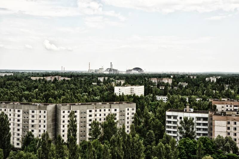 vervallen flats in Tsjernobyl overwoekerd door bomen met de kerncentrale op de achtergrond