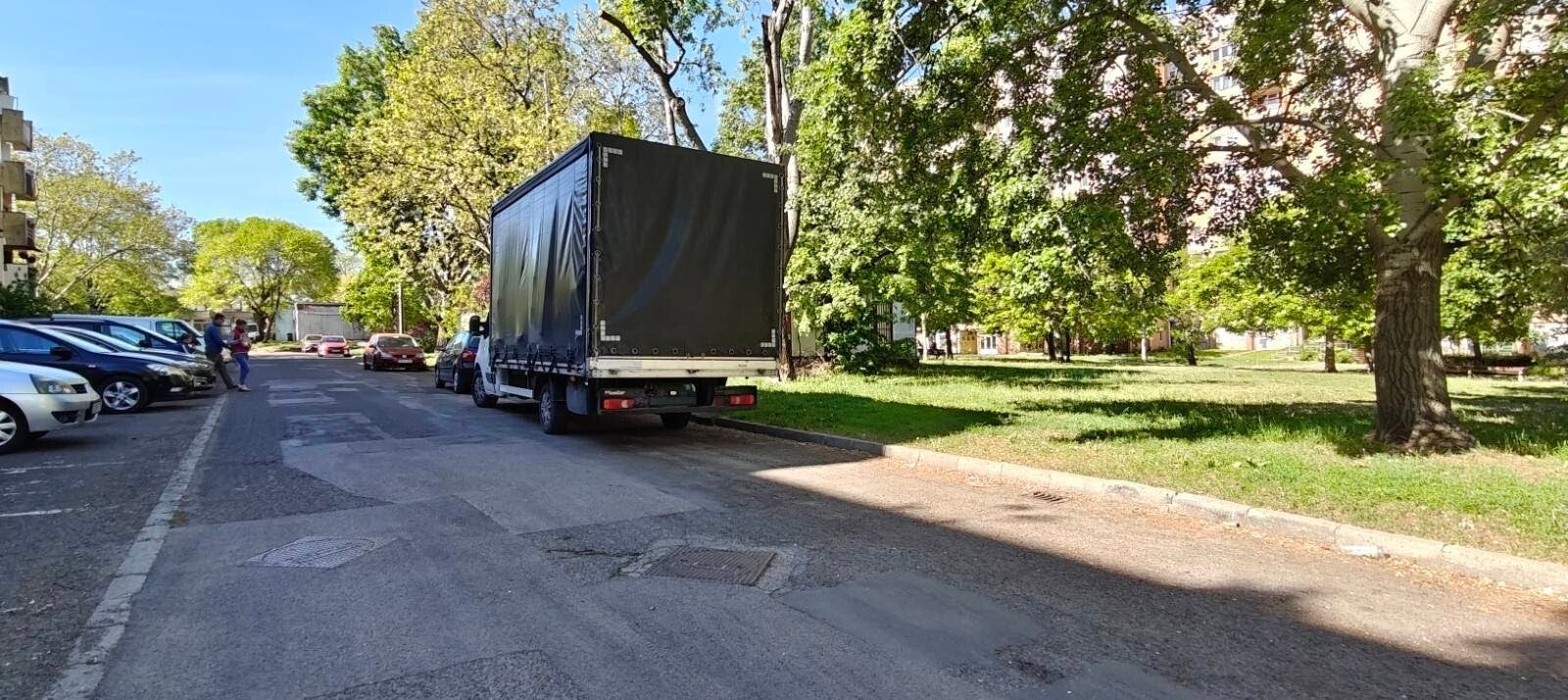 Biztosfuvar teherautója hátulról amint egy fás utcában várakozik