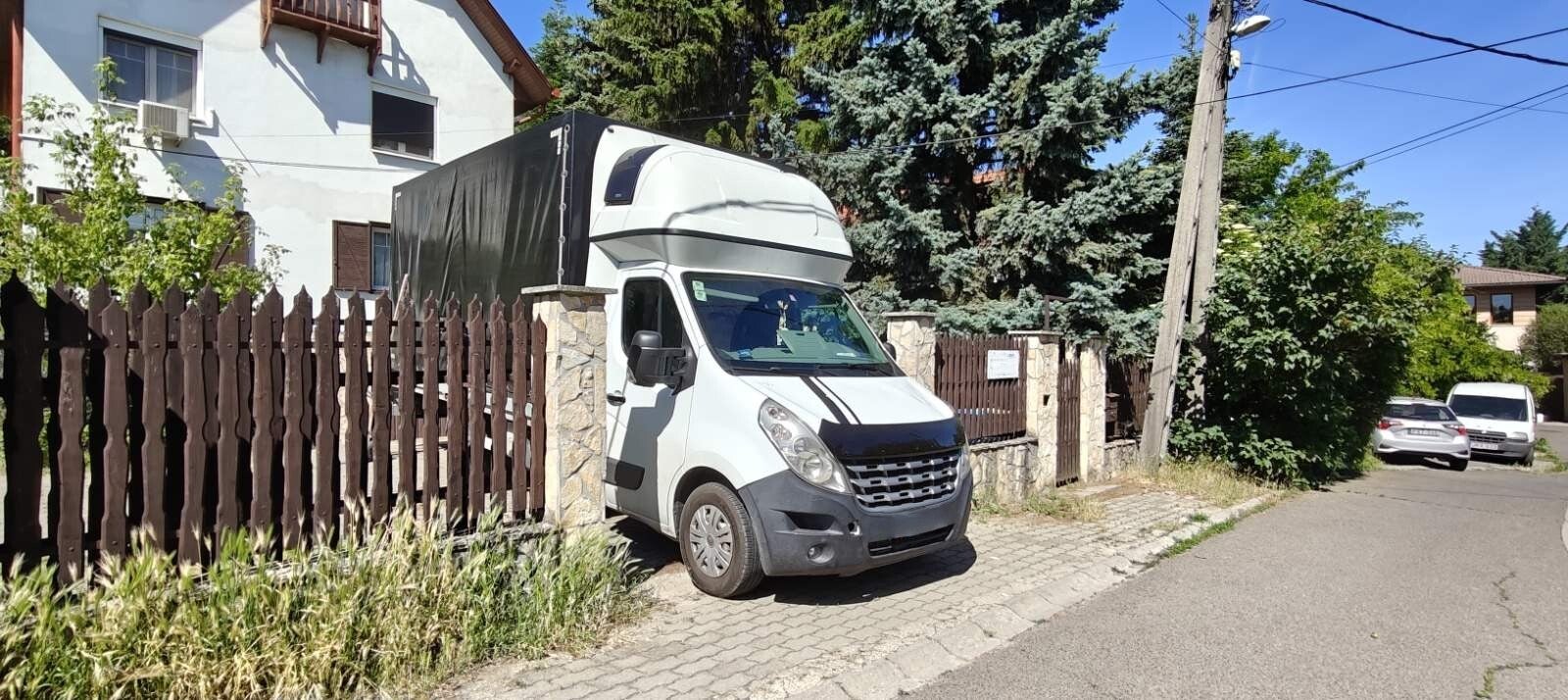 Biztosfuvar ponyvás kisteherautó egy kertes ház udvarában bepakoláskor