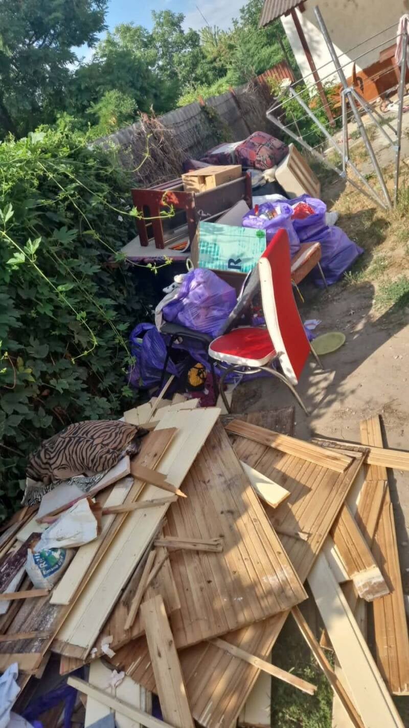 Kertes ház udvara, kidobált bútorokkal, fa lécekkel, hulladékos zsákokkal