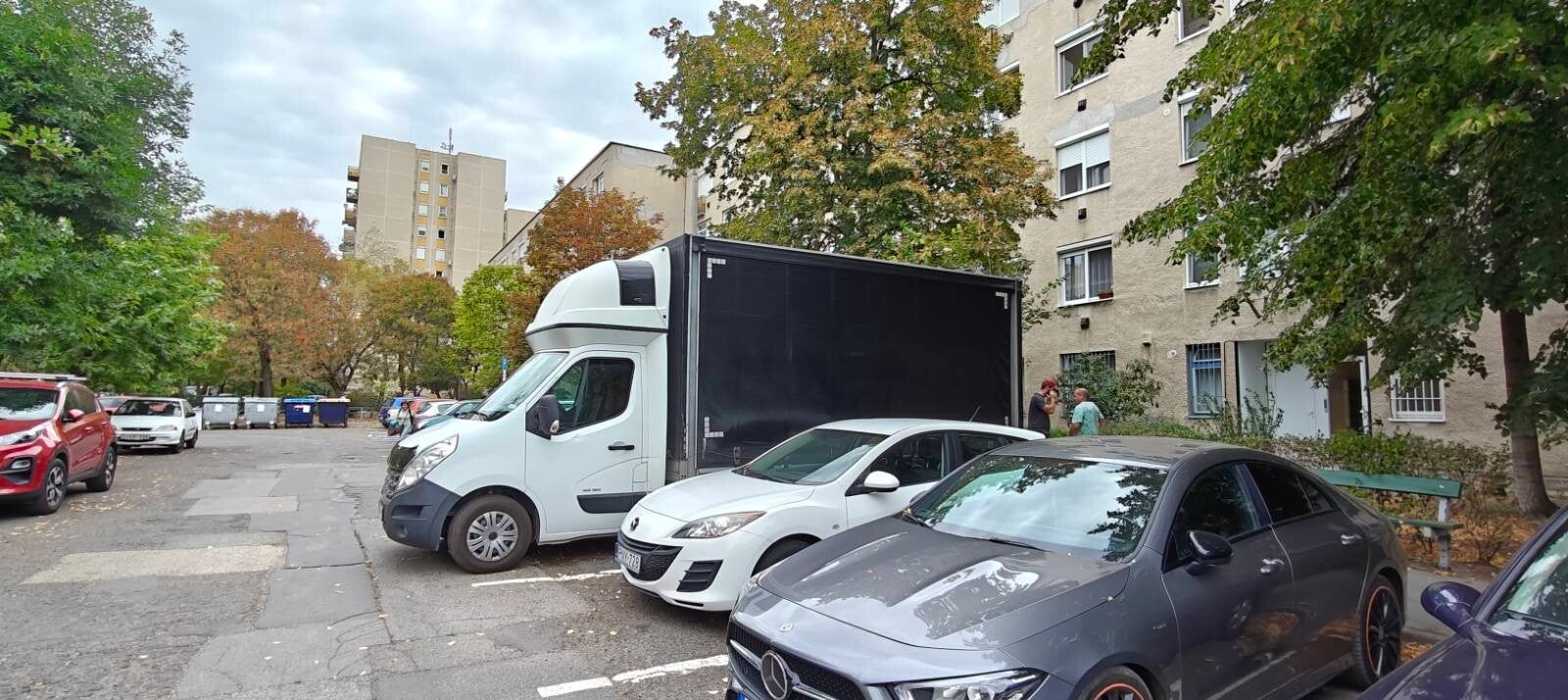 Ponyvás teherautó egy lakótelepi ház előtt parkol a parkolóban