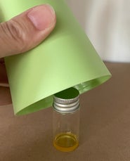 Kleine Glasflasche mit Leinöl-Firnis, lichtgeschützt durch einen übergestülpten Becher.