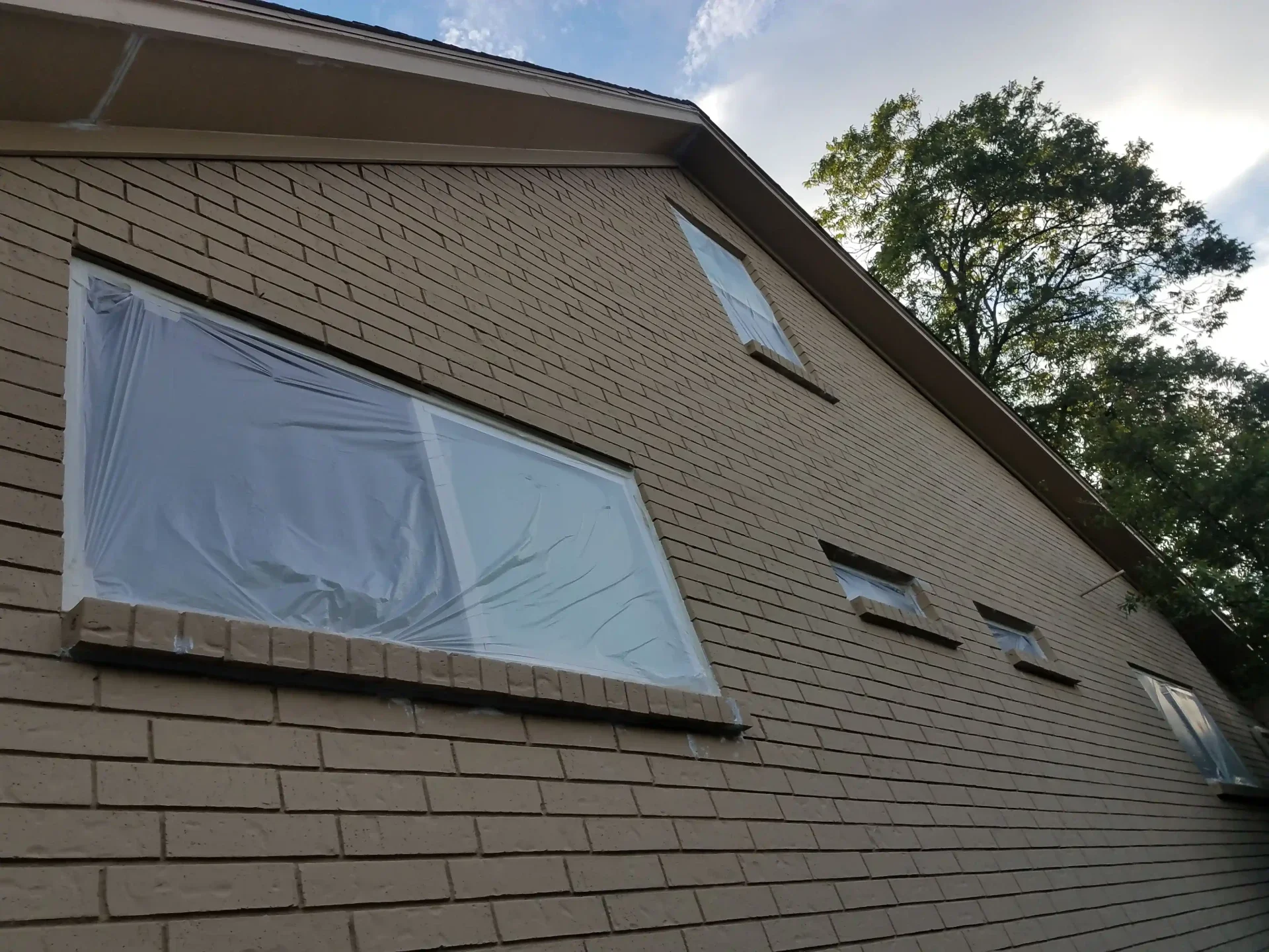 Exterior painting preparatino on brick , windows covered with painters plastic