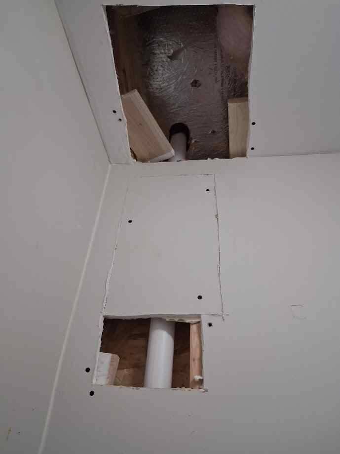 Drywall access holes in a wall and ceiling exposing plumbing pipes before repair, showing areas opened for plumbing work and ready for drywall patching and finishing.
